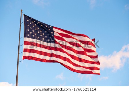 Giant American Flag flying high against a light blue sky with a couple of small clouds with room for text.