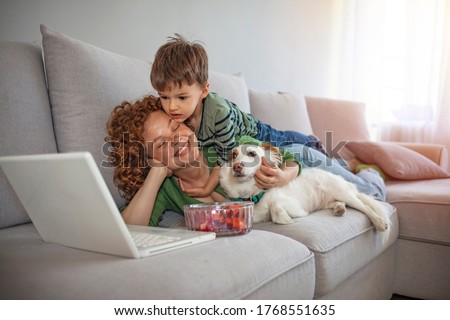 Smiling mother with her son using laptop close up, happy mum and little boy with dog sitting on sofa at home, watching cartoons online or play video game, family having fun