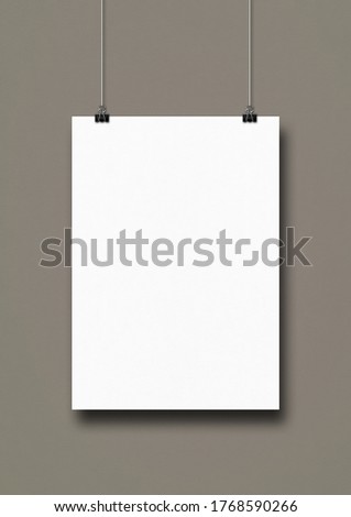 White poster hanging on a grey wall with clips. Blank mockup template