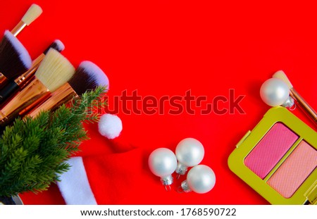 creative Christmas cosmetics flat lay - premium makeup brushes, blush palette Christmas balls, Christmas tree and Santa hat on a colored red background