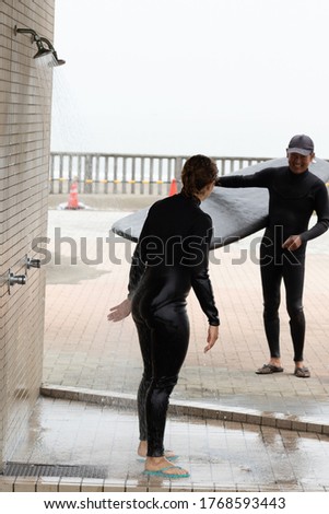 Young multiracial African American lady with amazing smile, freckles & frizzy hair & a Japanese surf instructor ob the beach after a surf lesson in Chiba Japan in a black wetsuit.