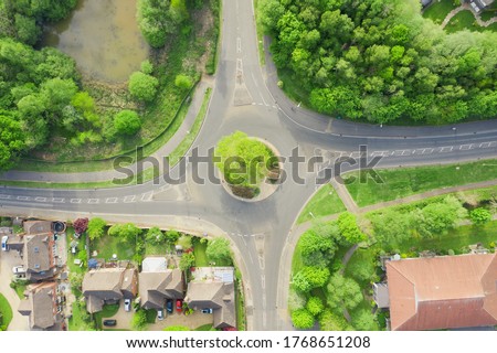 Round a bout on a housing estate in the United Kingdom. No cars driving, with road markings showing cars drive on the left. Houses with parked cars in a area with many trees. Royalty-Free Stock Photo #1768651208