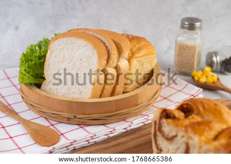 Bread in a wooden tray on a red and white cloth with lettuce and corn.