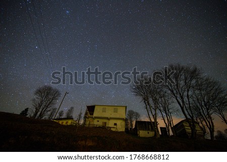 photo of a house taken at night with long exposure technique, silhouette of trees, stars and sky