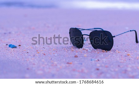 Sunglasses placed on the sand of the beach, close to the sea and ocean waves in summer.