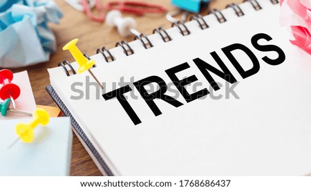 Trends text written in a notebook on a wooden table. View from above.