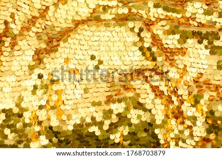 Background from golden scales. Mermaid's tail. Fashion shiny fabric. Scales of round sequins. Holiday abstract glittery background. Festive disco backdrop. Golden snakeskin. Color 2021