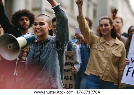 Young rebellious woman with megaphone during street protest. Female protestor yelling over a bullhorn as she participates in a street demonstration. Royalty-Free Stock Photo #1768719704