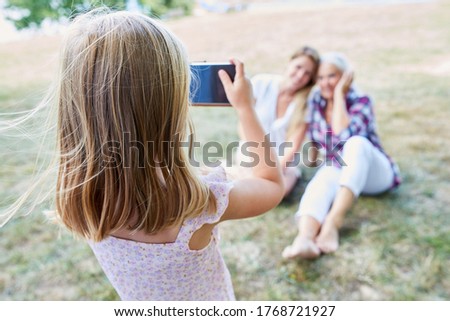 Little girl takes a picture with the smartphone from her mother and grandmother