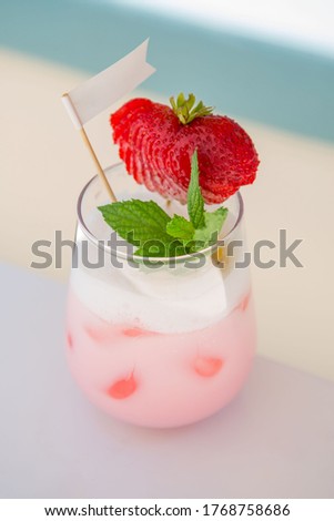 strawberry cocktail in front of a white background. cold pink cocktail with ice on the beach club in hot summer day. cocktail image with foam on the background with white and blue floor. 