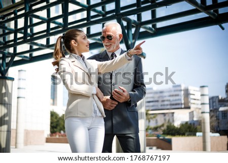 An older businessman in an elegant suit and his beautiful young associate are talking during a work break