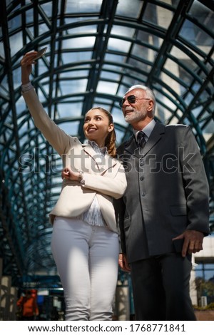 An older businessman in an elegant suit and his beautiful young associate are takeing sefie during a work break