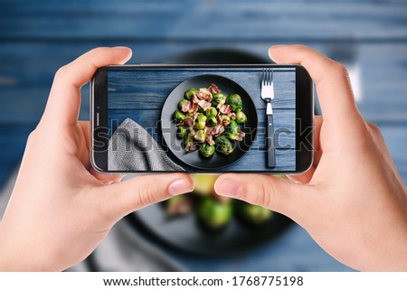 Blogger taking picture of delicious Brussels sprouts with bacon at table, closeup. Food photography