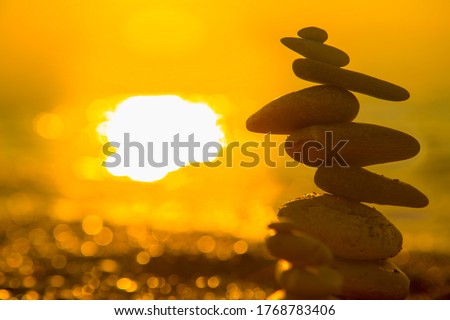 Balanced Pebbles Pyramid on the Beach on Sunny Day and Clear Sky at Sunset. Blue Sea on Background Selective focus, zen stones on sea beach, meditation, spa, harmony, calm, balance concept

