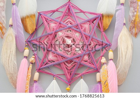 Close up mandala dreamcatcher with pink purple golden feathers on gray background