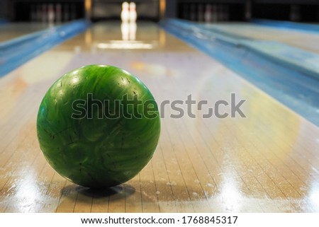 green round bowling ball in front of the throw on the track with two pins . bowling game
