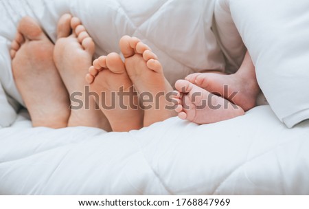 Legs of a family covered with a plaid closeup. Mom, daughter and newborn son are lying, sleeping under a white blanket. Photography, concept.