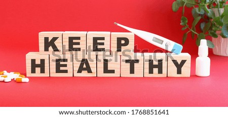 The word KEEP HEALTHY is made of wooden cubes on a red background with medical drugs. Medical concept.