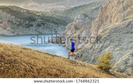 man athlete running uphill background of sea bay and rocks in sunset