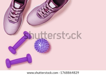 Sneakers, dumbbels and massage ball on pink background. Flat lay picture.