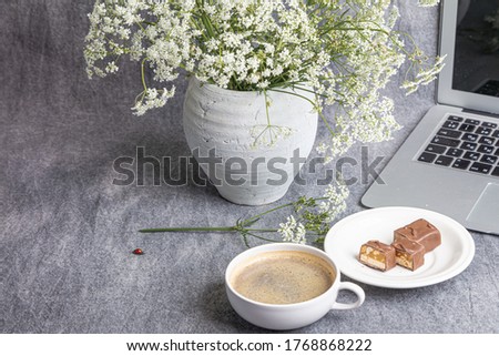 Still life: laptop, a vase with white flowers, a cup of coffee on a gray background