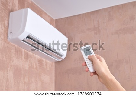 air conditioner at domestic room. heat temperature indoors. person holds remote control for aircon. heat or cold at home. Royalty-Free Stock Photo #1768900574