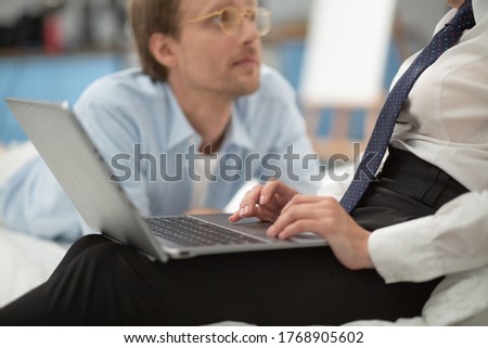 Man laying near his wife while she is working. Close up shot of businesswoman hands typing on laptop. Young ladys tender hands working on computer while her boyfriend watches her blurred in background