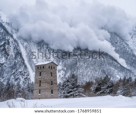 Descent of an avalanche from the mountain. House at the foot of the mountain. Winter mountain landscape. Royalty-Free Stock Photo #1768959851