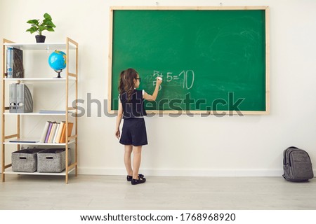 Back to school. Rear view of a schoolgirl in chalk writes on a school chalkboard in class.