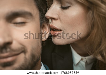 Woman kisses or whispers in man's ear. Selective focus on female lips near male ear in the center of image. Passionate couple in love. Close up shot. Royalty-Free Stock Photo #1768987859