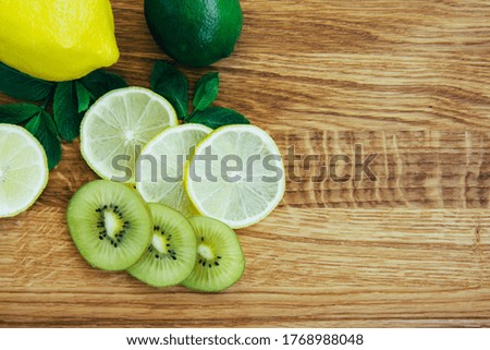 Yellow lemon and green lime, kiwi, mint leaves on a wooden board. A large knife next to a cutting board. Tropical fruits on light brown wooden background. Fresh citrus. Space for text. Top view