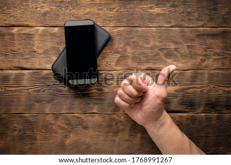 Wireless charger and mobile phone in male hand on a wooden table background.