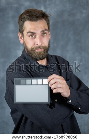 The model holds a color card in its hands for correct color transfer during further color correction. Closeup of a Colorchecker card in the hands. Neutral grey