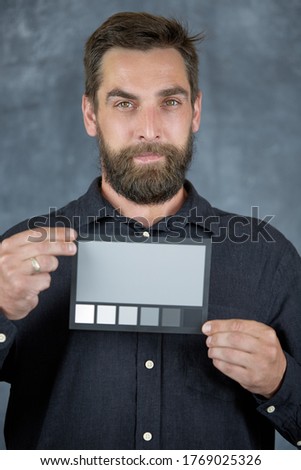 The model holds a color card in its hands for correct color transfer during further color correction. Closeup of a Colorchecker card in the hands. Neutral grey