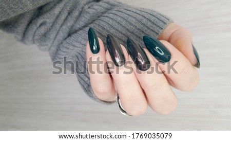 Woman's hand with long nails and green manicure with bottles of nail polish