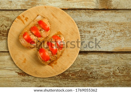 Chicken breast in marinade stuffed with tomatoes on a round wooden board. Copy space.