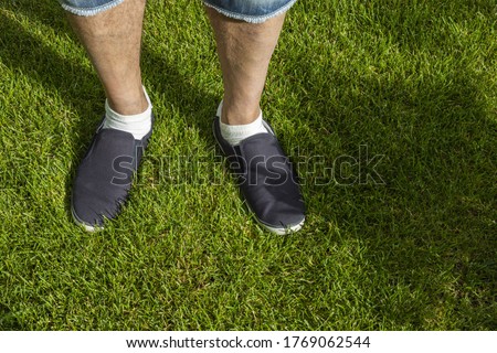 Close up view of male feet in black sneakers on green grass lawn on sunny day. Summer men shoes.