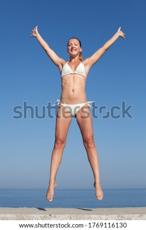 Jumping girl. Attractive young woman in white bikini hopping on seafront