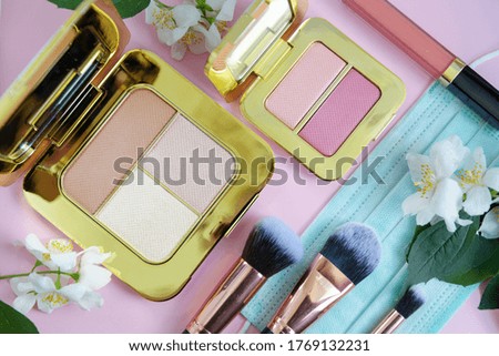 premium makeup brushes, eyeshadow palette, blush and a protective face mask on a colored pink background, creative cosmetics flat lay