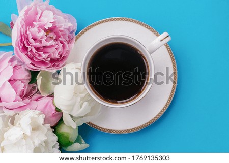 White cup of coffee,white and pink peonies on a blue background.Summer romantic breakfast.Good morning concept.Selective focus, top view