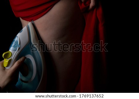 hand holds the iron and strokes the leg of a woman who has cellulite. photo in a dark key.