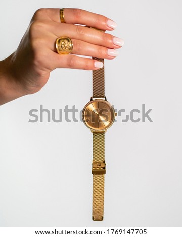 A vertical shot of a woman wearing two rings holding a gold watch n front of a white background