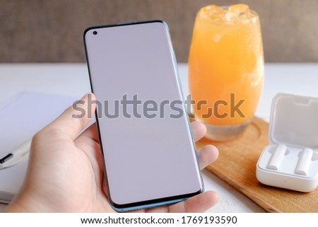 Asian men hold smartphones on the white wood table with books, pens, orange juice and earphones