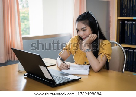 Teenager student studies online via laptop. University student girl watches online classes and writing a syllabus in notebook. Concept of distance study, online learning, webinars. Stock photo.