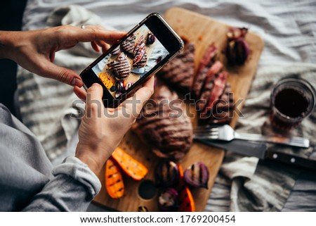 Taking a picture of some steaks and grilled vegetables with a mobile phone.