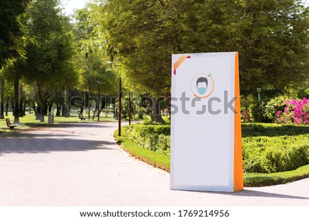 White advertising board in the park. Mask is Mandatory illustrated on the board. Safety measures to prevent coronavirus spread. 