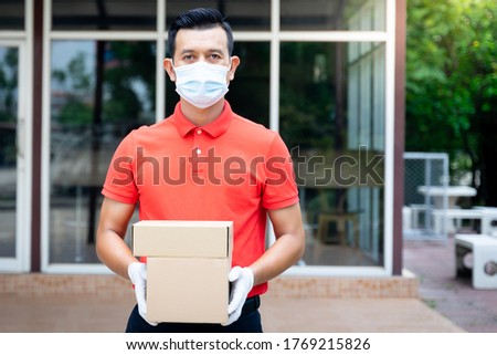 Delivery man employee in face mask and shield delivers parcels and box post to customer order online shopping during COVID-19 pandemic. Stock photo