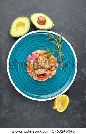 Salmon tartare with avocado, on a blue striped plate, with lime and croutons, against a dark background