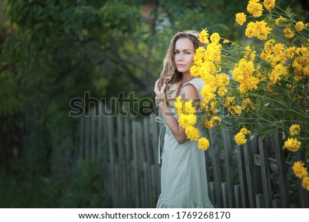 Girl stands at the fence on a background of yellow flowers. Image with selective focus and toning.