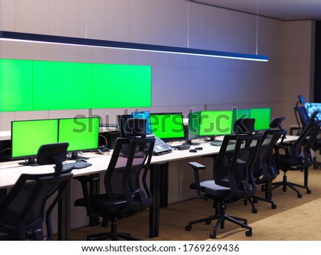 interior of big modern security system control room with blank green screens, workstation with multiple displays, monitoring room with at security data center  Empty office, desk, and chairs at a main